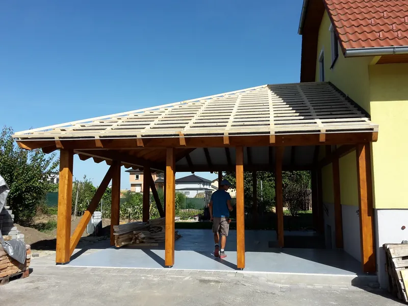 Carport mit Walmdach und Holzstützen vor einem Wohnhaus