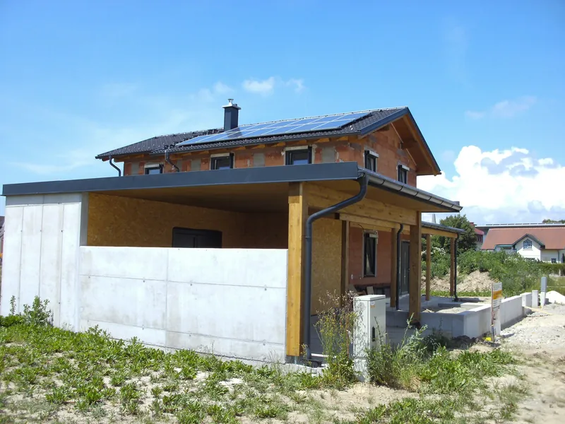 Carport mit dunkler Dachfläche neben einer Betonwand