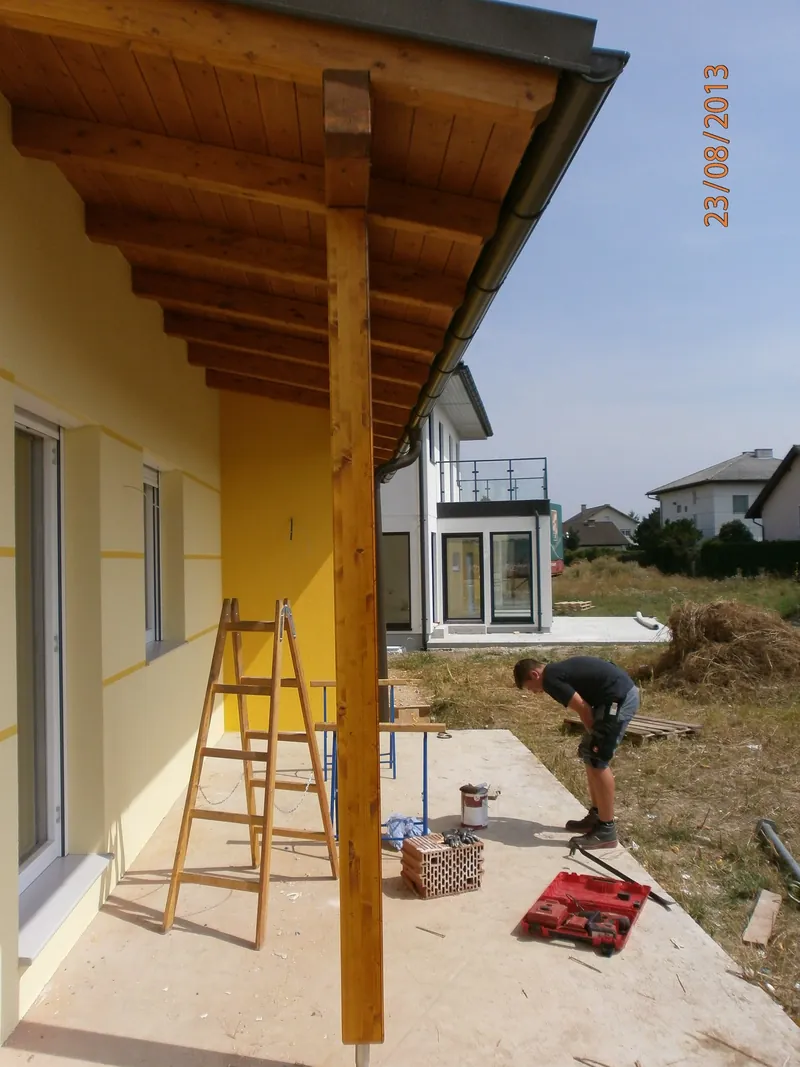 Holzüberdachung mit sichtbaren Sparren an einer gelben Fassade