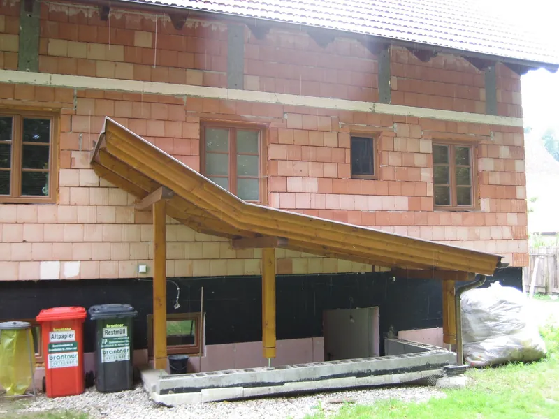 Geschwungenes Holzvordach an einem Ziegelhaus